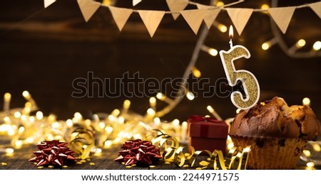 Number 5 gold burning candle in a cupcake against celebration wooden background with lights. Birthday cupcake. Copy space. Banner