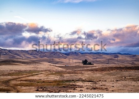 Agricultural atmospheric landscape with farmland with plowed fields and sloping meadows in a valley framed by a mountain range against the background of a cloudy evening twilight sky in California