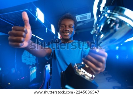 Concept cyber sport. Happy player young african man holding gold winner cup professional gamer online games computer, neon colour.