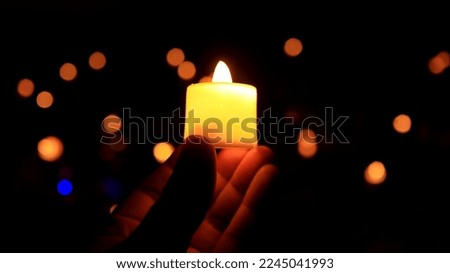 Defocused image, holding a burning candle against a dark background