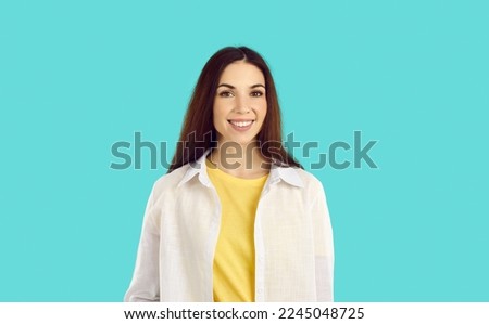 Portrait of beautiful smiling casual woman smiling on light blue background showing her white teeth. Close up of caucasian young brown-haired woman in casual t-shirt and shirt smiling at camera.