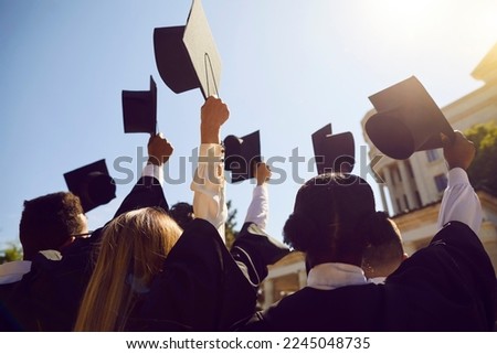 Students who finished studies raise hats high in air on graduation day. Confident graduates of prestigious university together raise hands with square academic caps up to bright blue sky in sun light Royalty-Free Stock Photo #2245048735