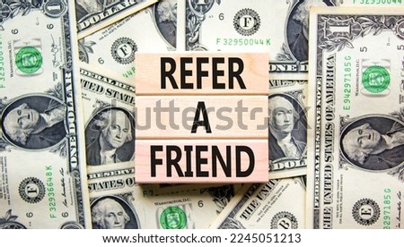 Refer a friend symbol. Concept words Refer a friend on wooden blocks on a beautiful background from dollar bills. Business and refer a friend concept. Copy space.