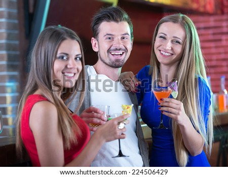 Portrait of happy friends holding glasses with cocktails in bar