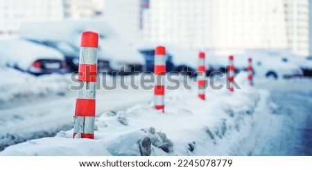Plastic reflective road cones in pole shape mounted on snowy winter urban street against cars parking lot. Road safety concept.