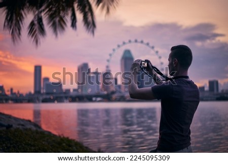 Man photographing Singapore urban skyline at beautiful sunset. Tourist with camera in modern city. 