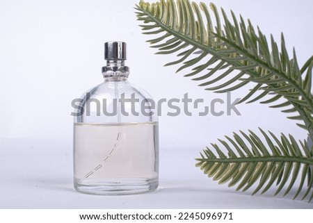top view of bottle of perfume surrounded with flowers and green leaf on white