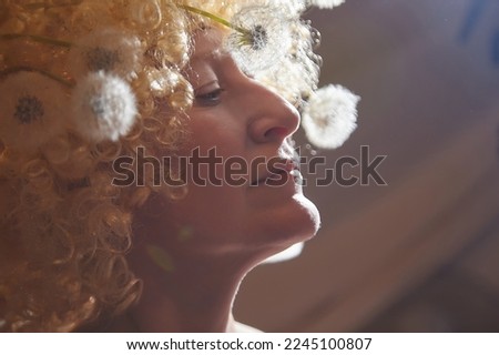 Portrait of woman in white blonde wig with dandelions. Female model posing in studio for dark picture