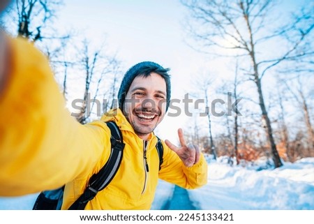 Happy man with backpack taking selfie portrait in winter frosty forest - Smiling hiker climbing mountains - Sport, travel and technology concept