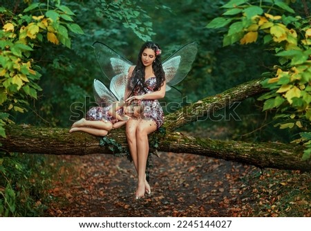 Fantasy woman fairy, sitting on log stroking with love sleeping little girl. Pixie is dreaming. Mom reads fairy tale to daughter, sings lullaby. family shooting motherhood care. trees summer forest Royalty-Free Stock Photo #2245144027