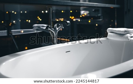 Steel faucet in the interior of a modern bathroom with a window overlooking the night city.