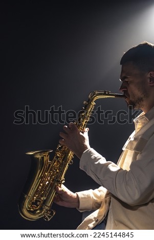 Male musician on stage plays the saxophone dark with smoke, copy space.