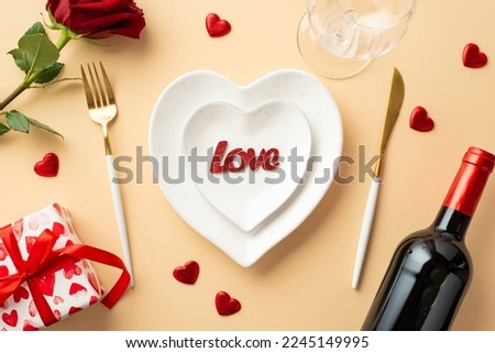 Valentine's Day concept. Top view photo of heart shaped dishes with inscription love cutlery wine bottle wineglass rose and giftbox on isolated pastel beige background