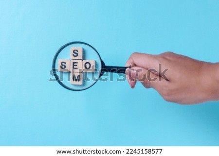 Hand holding magnifying glass look up SEO and SEM  word, Search Engine Optimization on a blue background.