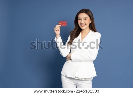 Happy young Asian business woman smiling and showing credit card for paying online business isolated on blue background Royalty-Free Stock Photo #2245181503