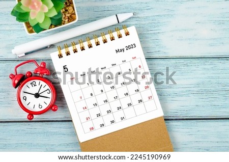 May 2023 Monthly desk calendar for the organizer to plan 2023 year with alarm clock and pen on wooden table.
