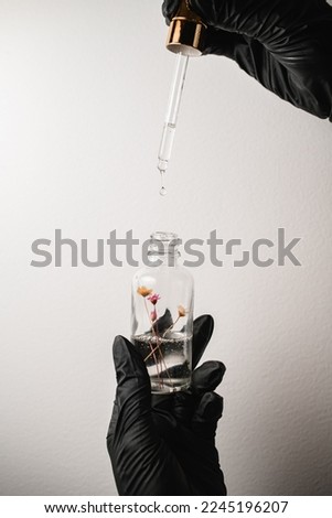 view of cosmetic dropper glass bottle with pipette and liquid inside it in female hands in black gloves.