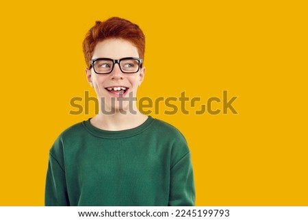 Portrait happy smiling red-haired confident boy in transparent glasses with a funny expression looks away, dressed in a green sweater. Isolated studio photo on a bright yellow background. Royalty-Free Stock Photo #2245199793