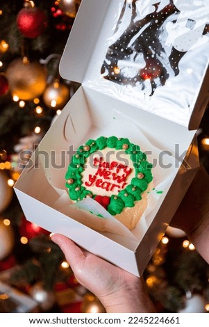 small bento cake with a New Year's cream picture near Christmas tree close up. trendy bakery.   