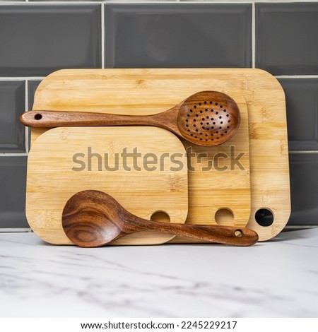 stack of bamboo chopping boards and teak hardwood spoons lined up against grey tiled walls Royalty-Free Stock Photo #2245229217