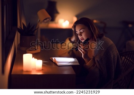 Young woman reading book with flashlight at home during blackout Royalty-Free Stock Photo #2245231929