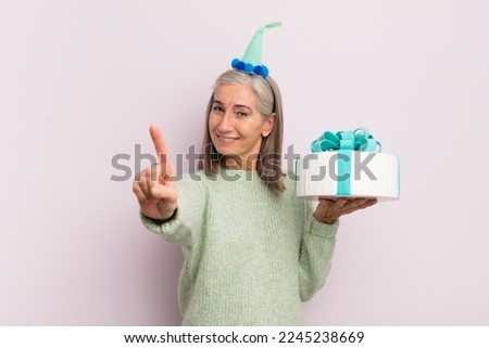 middle age woman smiling and looking friendly, showing number one. bitrthday cake concept
