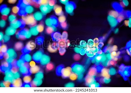Colorful lights bokeh from decorative luminous flowers garlands at holiday, blurred festive background, abstract outdoor lights with boke. Multicolored flowers lights with beautiful bokeh at night