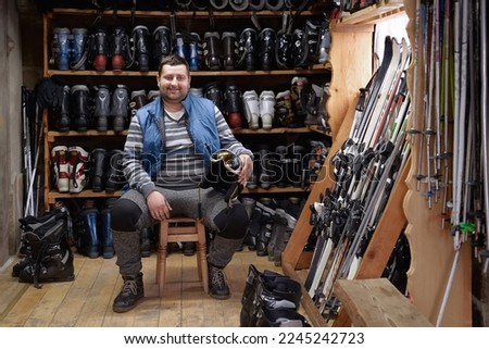 Ski rental service. Cheerful small business owner man with skis, ski boots, helmets, and other winter sport equipment for rent or sale