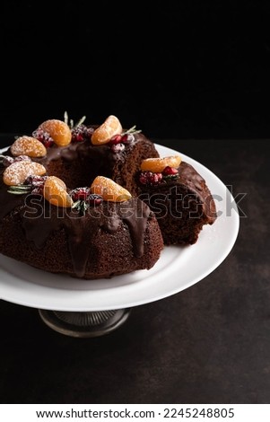 Blurred image of a chocolate cupcake decorated with tangerine slices, pomegranate berries, rosemary sprigs on a dark background. Holiday baking concept.