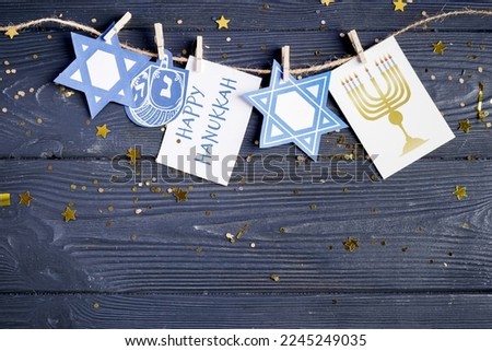 Card with text HAPPY HANUKKAH, pictures, clothespins and rope on dark wooden background