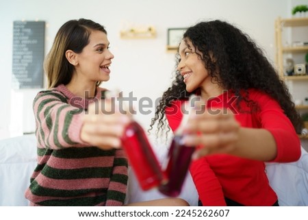 Caucasian white and African black ethnic women having a drinking together in celebrating event in their apartment bedroom. Woman colleague cheering and clinking a cocktail bottles.