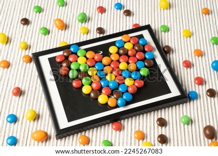A unique and eye-catching design with small colorful dragee candies arranged like a heart-shaped picture on a white table.