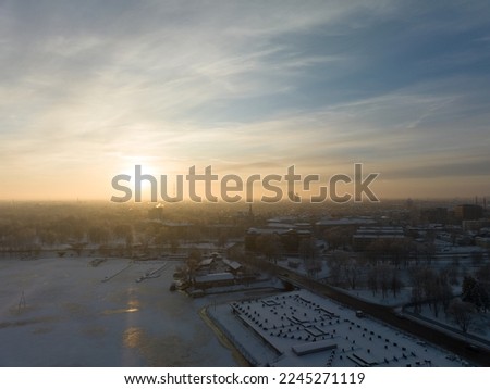  the sun is setting over a city with a lot of snow on the ground and buildings in the distance with a few clouds in the sky above the ground and in the foreground of the photo. . 