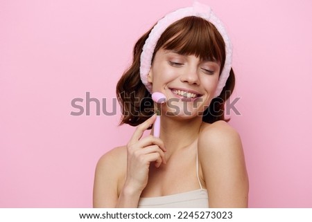a close photo of a happy, delighted woman, happily smiling, close her eyes and doing a massage with a pink roller