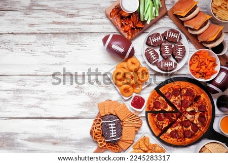 Superbowl or football theme food side border. Pizza, hamburgers, wings, snacks and sides. Overhead view on a white wood background. Royalty-Free Stock Photo #2245283317