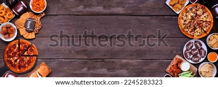 Superbowl or football theme food double border. Pizza, hamburgers, wings, snacks and sides. Top down view on a dark wood banner background. Royalty-Free Stock Photo #2245283323