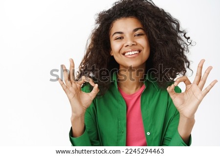 Positive smiling black girl, shows okay, ok sign in approval, says yes, likes and approves smth, white background