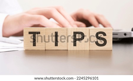 word TIPS made with wood blocks on the background man working of the laptop. selective focus.