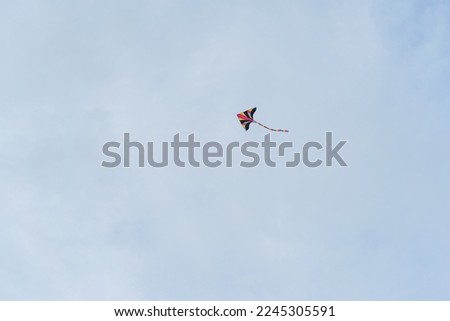 A photo of a small colorful kite flying high in the sky. The photo was taken on Naiyang Beach in Thailand. 