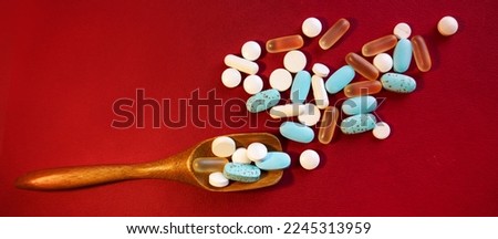 The tablets lie in a measuring wooden spoon and are scattered on a red background. The concept of healthcare and medicine.