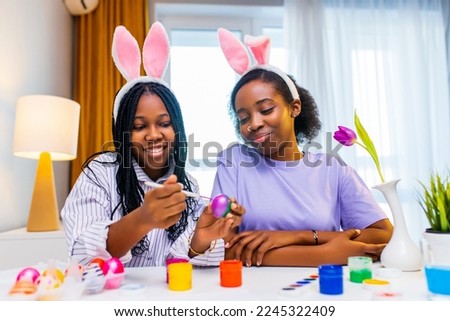 two happy sister with bunny ear painting eggs in apartment preparing to easter