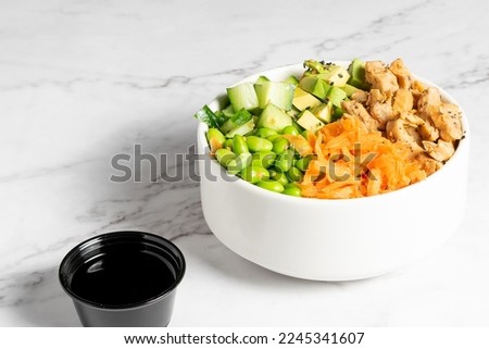 Chicken, carrot, cucumber and beans poke served in a white bowl on a marble table. High quality photo