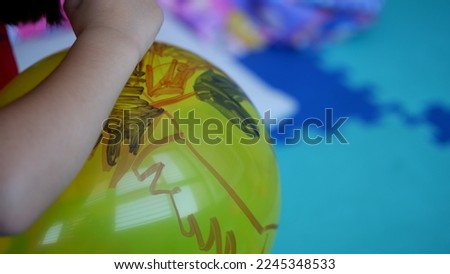 a little girl drawing on a yellow balloon. 