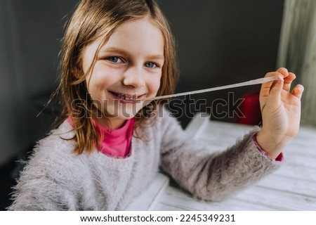 A beautiful smiling red-haired little girl, a child chews a sweet chewing gum and stretches it with his hand in length. Photography, portrait.