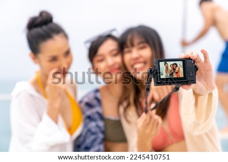 Group of Attractive Asian woman friends using digital camera photography together while travel on luxury private catamaran boat yacht sailing in the ocean on summer holiday vacation at tropical island