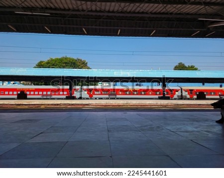 Stock photo of empty railway station or platform under gray color shelter, steel and wooden benches, drinking water taps for passenger at platform. red color train passes railway platform in India. Royalty-Free Stock Photo #2245441601