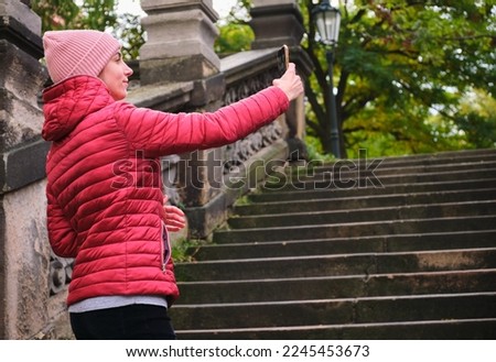 Portrait of woman red jacked pink fur cap taking selfie photo in park autumn