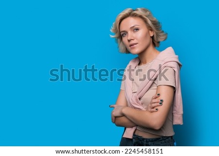 Studio shot of cute woman looking sideways with thoughtful and sly expression, isolated over blue background with copy space. Creative concept idea. Pensive Royalty-Free Stock Photo #2245458151