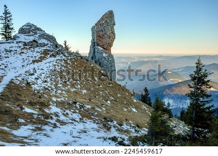 Natural rock formation cliff with anthropomorphic appearance, standing tall and alone on top of the mountain, above foggy valleys and hilly landscape background. Dramatic winter landscape, aerial view