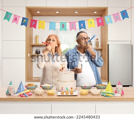 Mature man and woman at a birthday party blowing a horn behind a kitchen counter